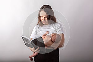 Beautiful young mother breastfeeding a baby while reading a black book