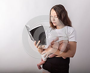 Beautiful young mother breastfeeding a baby while reading a black book