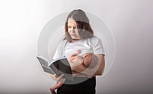 Beautiful young mother breastfeeding a baby while reading a black book