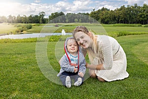 Beautiful young mother and cheerful 9 months old baby boy relaxing on grass at park