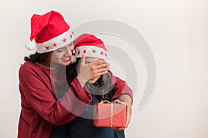 Beautiful young mother covering eyes of her daughter giving a present christmas on white background with copy space for text