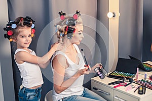 Beautiful young mother and her daughter with hair curlers