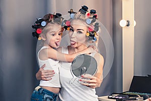 Beautiful young mother and her daughter with hair curlers are sp