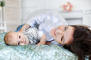 Beautiful young mother with her newborn baby son lying on bed in her bedroom.