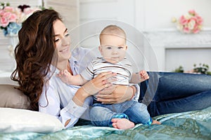 Beautiful young mother with her newborn baby son lying on bed in her bedroom.