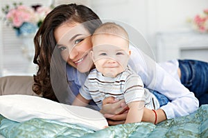 Beautiful young mother with her newborn baby son lying on bed in her bedroom.