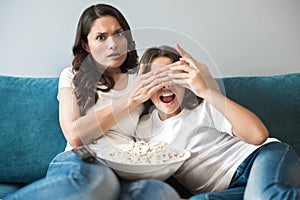 Beautiful young mother with her teenager daughter watching movie with violence scene mother closes child`s eyes