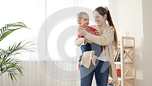 Beautiful young mother holding her baby boy and showing him toys in living room. Baby development, family playing games, making