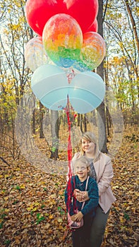 A beautiful young mother hugs her a little adorable daughter and holds the colorful balloons on a wall walk in autumn