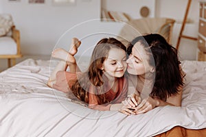 Happy cute little girl with a beautiful young mother lie on the bed