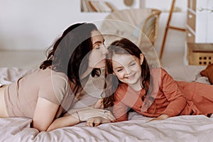 Happy cute little girl with a beautiful young mother lie on the bed