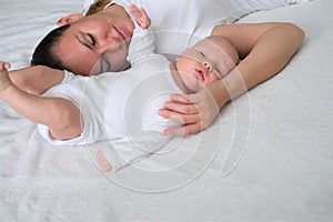 Beautiful young mother lies with her newborn baby on the bed.Portrait of mom and son in white clothes.