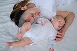 Beautiful young mother lies with her newborn baby on the bed.Portrait of mom and son in white clothes.