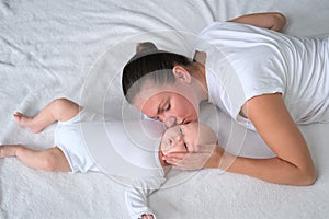 Beautiful young mother lies with her newborn baby on the bed.Portrait of mom and son in white clothes.