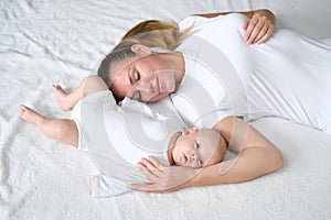 Beautiful young mother lies with her newborn baby on the bed.Portrait of mom and son in white clothes.