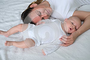 Beautiful young mother lies with her newborn baby on the bed.Portrait of mom and son in white clothes.