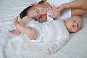 Beautiful young mother lies with her newborn baby on the bed.Portrait of mom and son in white clothes.