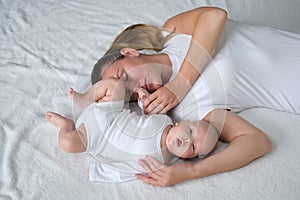 Beautiful young mother lies with her newborn baby on the bed.Portrait of mom and son in white clothes.