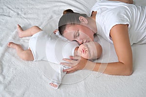 Beautiful young mother lies with her newborn baby on the bed.Portrait of mom and son in white clothes.