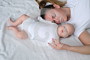 Beautiful young mother lies with her newborn baby on the bed.Portrait of mom and son in white clothes.