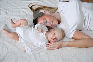 Beautiful young mother lies with her newborn baby on the bed.Portrait of mom and son in white clothes.