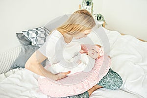 A beautiful young mother with long blonde hair and a daughter of 2-3 months are resting on the bed in the bedroom