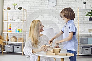 Beautiful young mother playing board game with her son at home. Parent and child building tower from wooder blocks