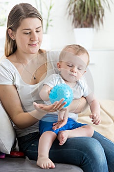 Beautiful young mother playing with her baby boy on sofa with ba