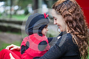 Beautiful young mother playing outdoors with her little baby girl wearing a ladybug costume. Halloween concept. Motherhood concept