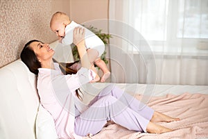 A beautiful young mother plays and cuddles with her baby in her bedroom on the bed. Love. motherhood Weasel tenderness