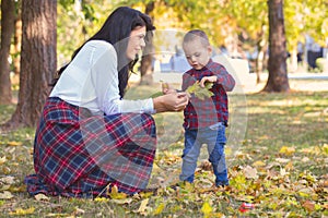 Beautiful young mother plays with her son in the park in autumn