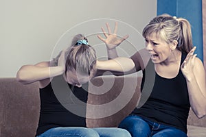 Beautiful young mother is scolding her daughter while sitting on sofa at home. Girl is covering her ears