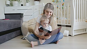 Beautiful young mother sitting on floor with her baby son and showing him family photographs in photo album