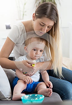 Beautiful young mother sitting on sofa and feeding her baby with