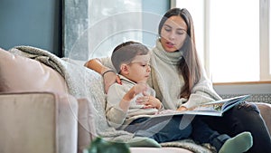 Beautiful young mother sitting on the sofa in your house the living room reads son a story in the ear and learn to read