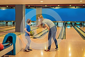 beautiful young mother and son playing bowling with medical masks during COVID-19 coronavirus in bowling club