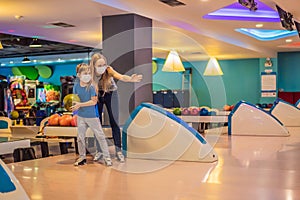 beautiful young mother and son playing bowling with medical masks during COVID-19 coronavirus in bowling club