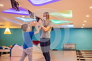 beautiful young mother and son playing bowling with medical masks during COVID-19 coronavirus in bowling club