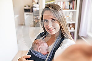 Beautiful young mother with son in sling taking selfie