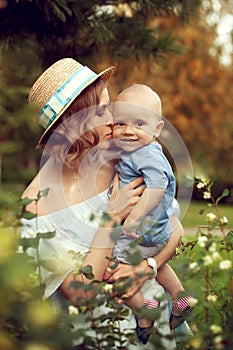 Beautiful young mother in summer hat kisses baby in the summer o