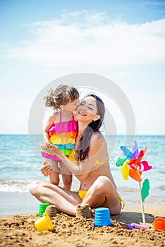 Beautiful young mother in swimsuit and a small 3 year daughter with a multi-colored pinwheel rainbow on the sandy beach at sea.