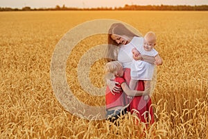 Beautiful Young mother with two children walking through wheat field. Weekend in countryside
