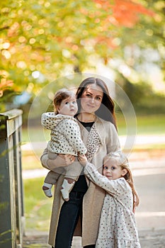 Beautiful young mother with two small children walks in the autumn park. Portrait of a happy family. Fall
