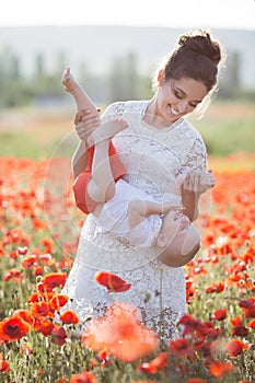 A happy mother with a small son in her arms on the endless field of red poppies on a sunny summer day photo