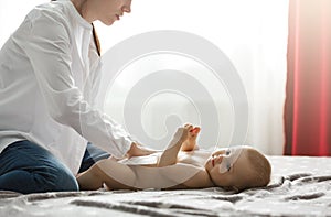 Beautiful young mother in white shirt and jeans putting diaper on cute newborn baby preparing for family dinner with