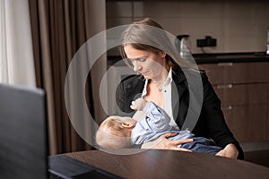 A beautiful young mother is working with a laptop and breastfeeding her newborn baby at home. Mom is a business woman