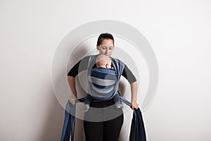 Beautiful young mother wrapping her son into sling. Studio shot.