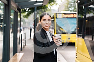 Beautiful young multiracial hispanic business woman using public transportation in city smiling and holding eco thermo