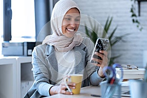 Beautiful young muslim business woman wearing hijab sending messages with mobile phone while sitting in the office