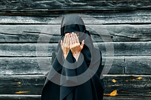 A beautiful, young, Muslim girl in a black veil with a closed face on the background of a gray tree prays. Copy space